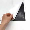 Folia magnetyczna w zbliżeniu pokazującym odklejanie białego papieru zabezpieczającego warstwę kleju
