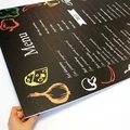 Tablica kredowa z przykładowym nadrukiem menu i grafiką warzyw trzymana w dłoniach w zbliżeniu na krawędź