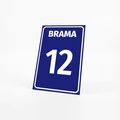 Granatowa tabliczka z białym napisem Brama i numerem 12, ustawiona na jasnym tle