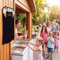 Tablica kredowa z nadrukiem cennika lodów i grafiką rożków, zamontowana na drewnianej ścianie budki gastronomicznej
