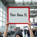 Tabliczka suchościeralna w czerwonej ramce z przykładowym napisem Pani Anna N. trzymana w dłoniach na lotnisku